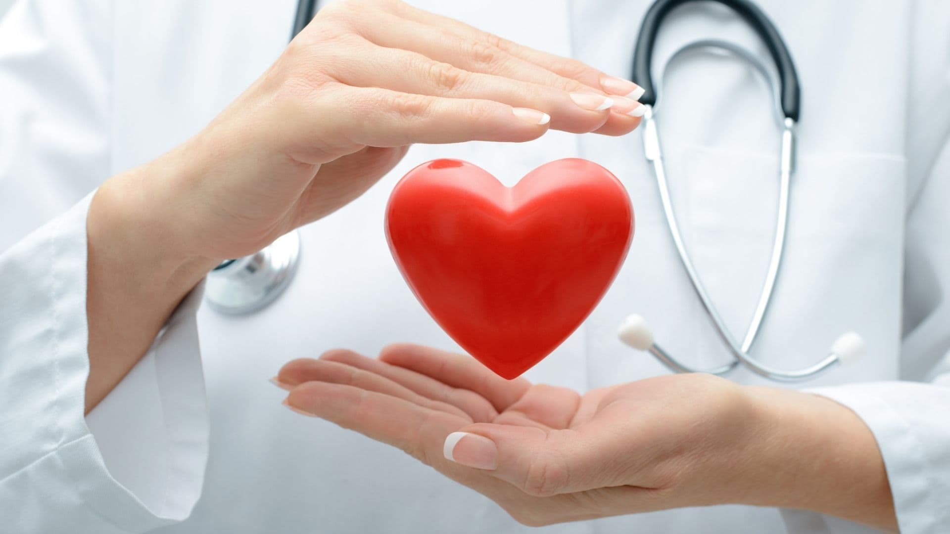 Doctor cradling a red heart with stethoscope, representing compassionate care
